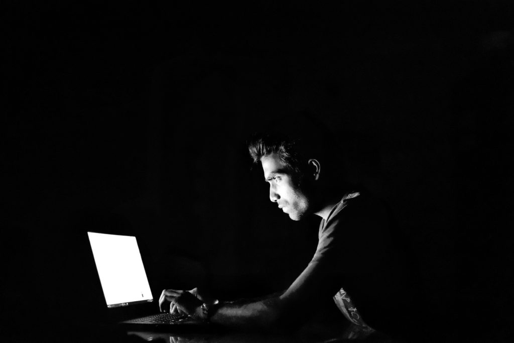 Mann sitzt im dunkeln vor dem Laptop.
